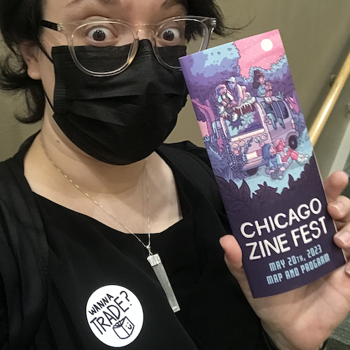 photograph of Alex holding up the Chicago Zine Fest program with a sticker on that says "Wanna Trade?"