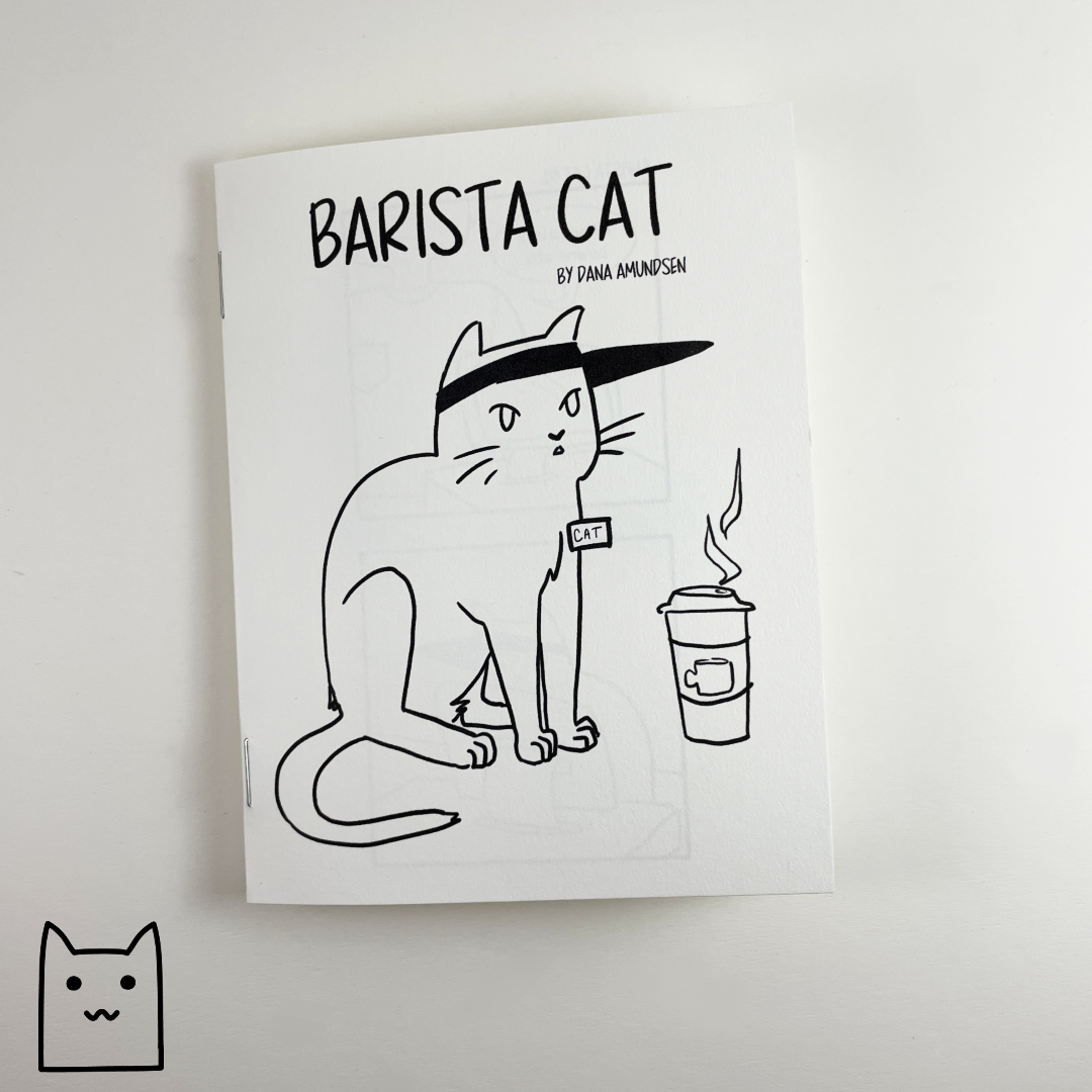 A photo of Barista Cat, a zine by Dana Amundsen. The cover shows a cat wearing a nametag and visor.